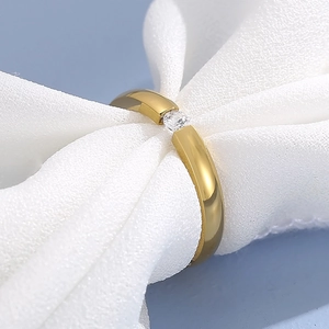 Macro detail of a minimalist gold ring with a sparkling round zircon on soft silk fabric