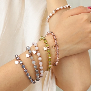 Layered beaded bracelets with natural stones, pearls, and a rose gold heart charm on a wrist