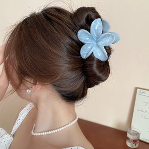 Gros plan d'une grande pince à cheveux fleur en acrylique bleu marbré sur un chignon