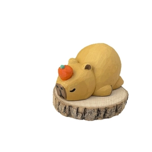 Handcrafted wooden capybara figurine with orange on head sleeping on wood slice base