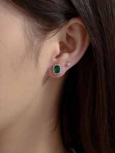 Close-up of emerald green rectangle stud earrings with halo diamonds on model