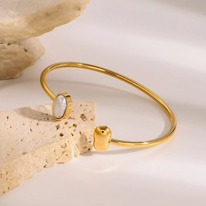 Detail of gold open bangle featuring white oval gemstone and polished metal ball