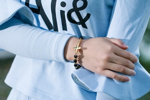 Détail du bracelet en perles noires avec un pendentif croix dorée poli au poignet