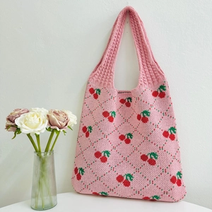 Pink knit tote bag with cherry and diamond patterns hanging on a white wall