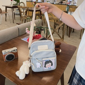 Sac bandoulière en toile bleu clair avec pendentif ours tenu à la main au café
