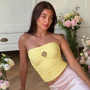 Detalle del top bandeau amarillo con broche de flor dorada y textura fruncida en tela elástica
