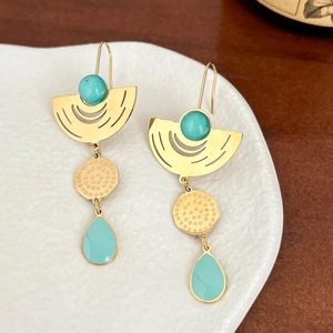Gold geometric earrings with turquoise enamel on white ceramic plate with wood background