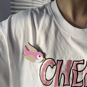 Close-up detail of cute handmade acrylic bird brooch in pink and white, worn on clothing.