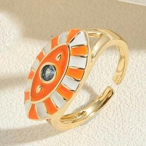 Close-up of gold evil eye ring with orange enamel and blue crystal on beige surface