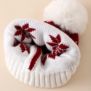Detailed knit texture of a red winter snowflake hat with a fluffy white faux fur pompom