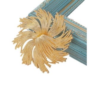 Elegant gold flower brooch with textured leaves on vintage blue frame background