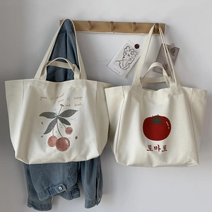 Detailed view of canvas tote bags with cherry and tomato prints on minimalist wood hooks