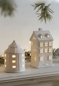 Detail of warm white glowing ceramic house ornaments with festive pine branch decor