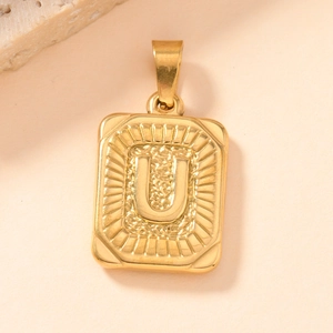 Macro shot of gold square pendant with embossed letter U and radiating textured edges