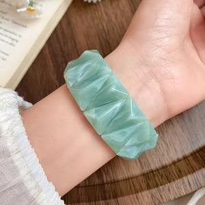 Close-up of light green faceted acrylic bangle on wrist with aesthetic vintage wooden background