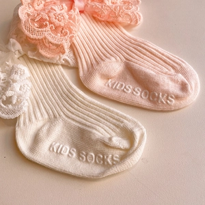 Detail view of baby lace socks with bow accents and non-slip textured soles in pink and white