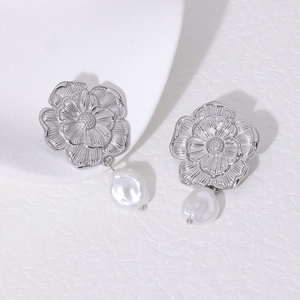 Detail of silver floral stud earrings with hanging white baroque pearl on textured surface
