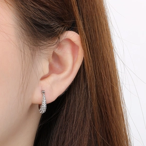 Close-up of elegant small silver hoop earrings with clear micro-pave crystals on the ear