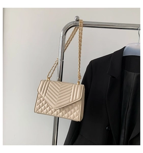 Close-up of beige quilted crossbody bag with V-shaped stitching and gold chain strap