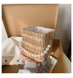 Detail of woven straw bag featuring pearl handle and detachable gold chain strap
