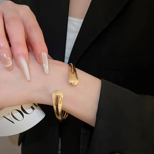Close-up of golden cross water-drop leaf open bracelet on model with black suit