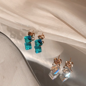 Detail of square sea blue and clear crystal stud earrings on satin with reflection