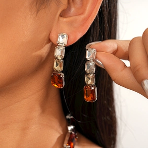 Close-up of long drop earrings with square amber and clear crystals on silver base
