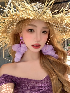Gros plan de grandes boucles d'oreilles fleurs en tissu violet portées par un mannequin