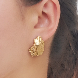 Close-up of golden irregular lava texture earrings on model's ear showing unique metallic finish
