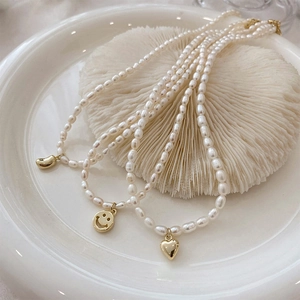 Detailed view of three freshwater pearl necklaces with smiley, heart, and gold bean charms