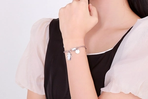Détail d'un bracelet argenté avec pendentif disque et petite fille sur le poignet d'un mannequin