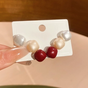 Close-up of pearlized square stud earrings set in white, beige, and dark red colors