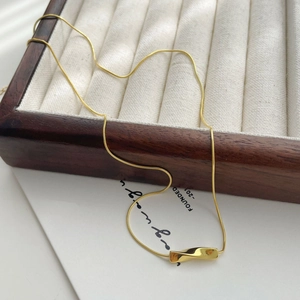 Close-up of golden snake chain with twisted bar pendant on velvet jewelry box