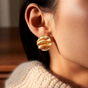 Close-up of 18k gold plated earrings with a hammered wave texture worn by a model