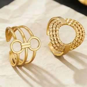 Detail of gold-plated geometric rings with textured heart pattern on warm beige background