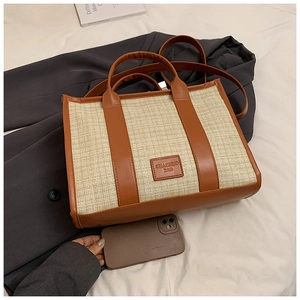 Straw and brown leather patchwork tote bag with shoulder strap on a white bed
