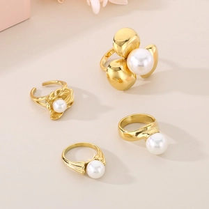 Dettaglio di quattro anelli placcati oro 18K con perle bianche su fondo beige