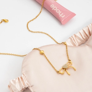 Detail showing gold bow necklace with diamond heart pendant on pink satin background