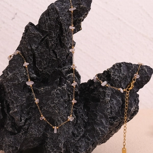 Detail of 18K gold-plated stainless steel chain with pink quartz stones on black rock
