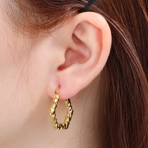Vue détaillée de boucles d'oreilles dorées en acier titane avec texture ondulée