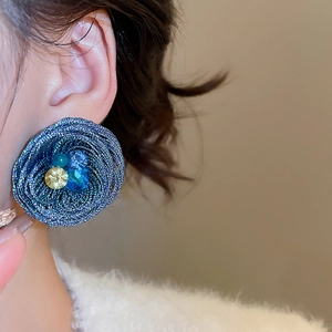 Detail of dark blue woven flower earrings with crystals worn by a model in close-up view