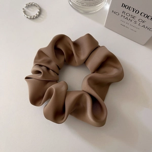 Detailed view of glossy brown satin scrunchie styled on a clean aesthetic tabletop
