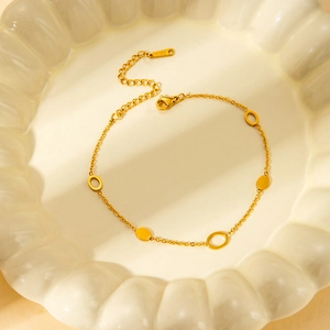 Detailed view of golden stainless steel bracelet with oval charms on white ceramic tray