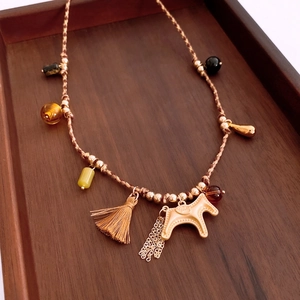 Detailed close-up of ethnic horse pendant necklace with brown tassels and wood tray display