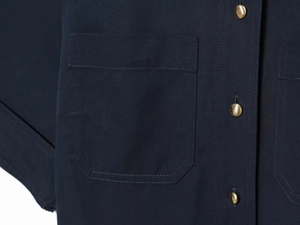 Détail de robe en sergé bleu marine montrant une poche à double couture et un bouton doré