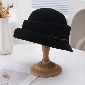 Elegant black straw bucket hat for women with a delicate bow on a wooden stand