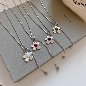 Silver wrinkled flower necklace with pearls and colorful stones on a textured book