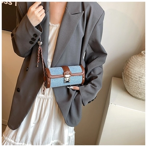 Detail of denim blue cylinder bag with brown leather trim and metal woven chain strap