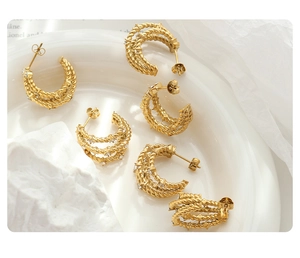 Macro view of gold multi-layer twisted C-shaped earrings with inlaid zircon on white porcelain