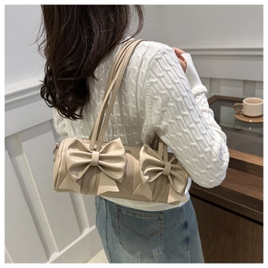 Model wearing a beige cylindrical shoulder bag with decorative leather bows
